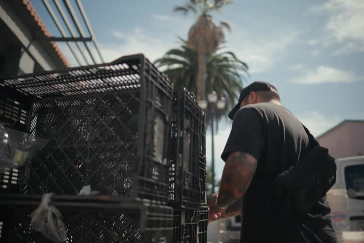 A man moving crates on the sidewalk at midday