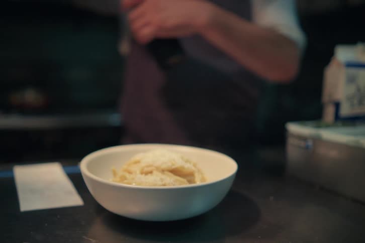 Restaurant kitchen worker adds cheese and pepper onto pasta dish