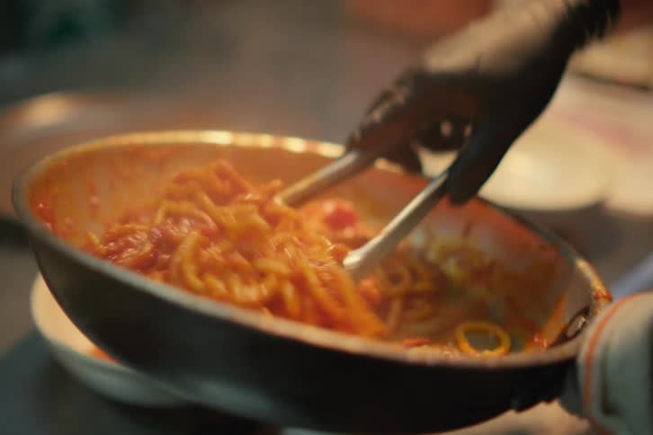 A pasta pan and a utensil being used to remove pasta from the pan