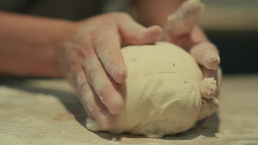 Close up of a person kneading dough over a table