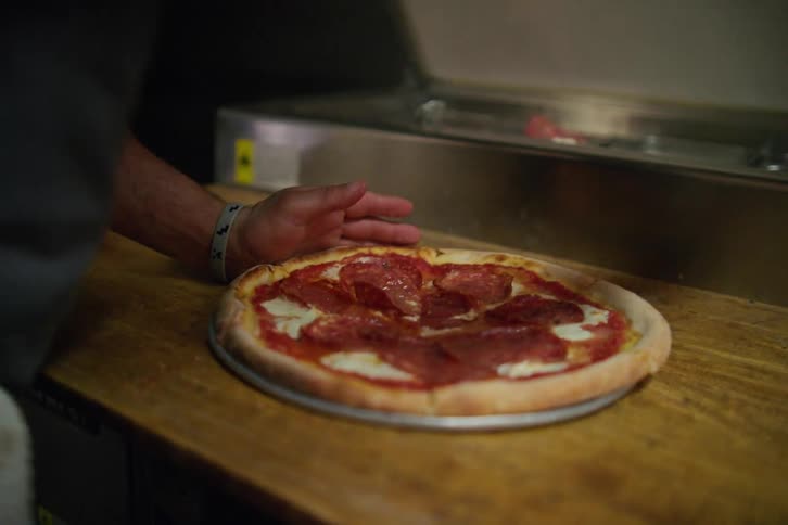 Chef cuts a small pepperoni pizza in a restaurant kitchen