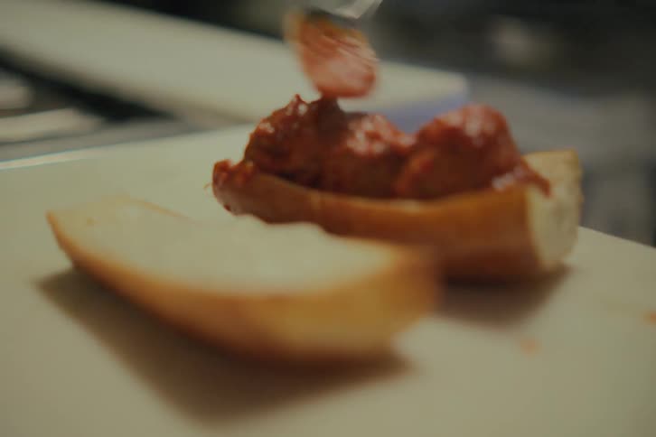 A person putting sauce and grated cheese on bread that is on the table
