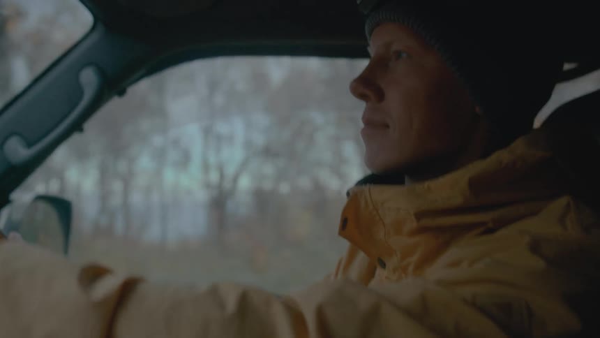 Man wearing a yellow jacket drives a car next to the forest