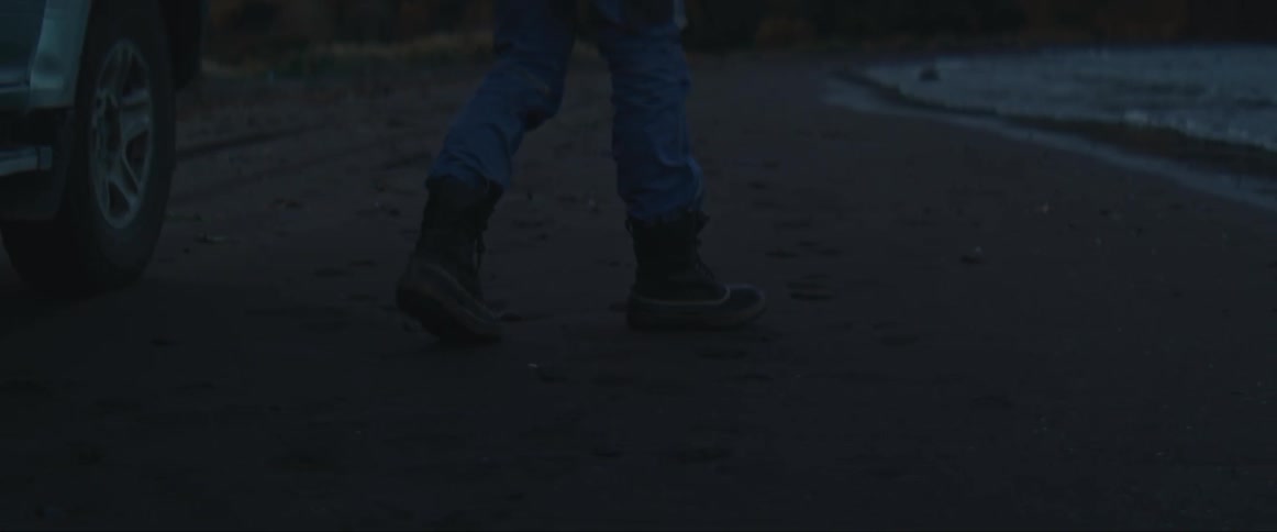 Man exits a car to stand next to the beach at evening