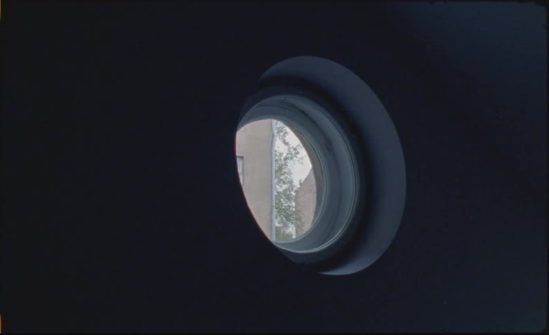 A dark room with a small circular window showing buildings outdoors