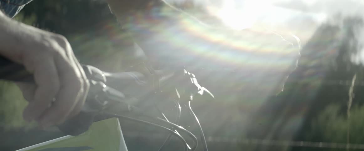 Rays of sunlight shine on hands on a dirt bikes handlebars