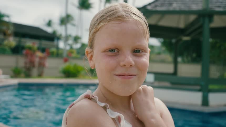 Close up of the face of a wet girl in a swimsuit next to the pool