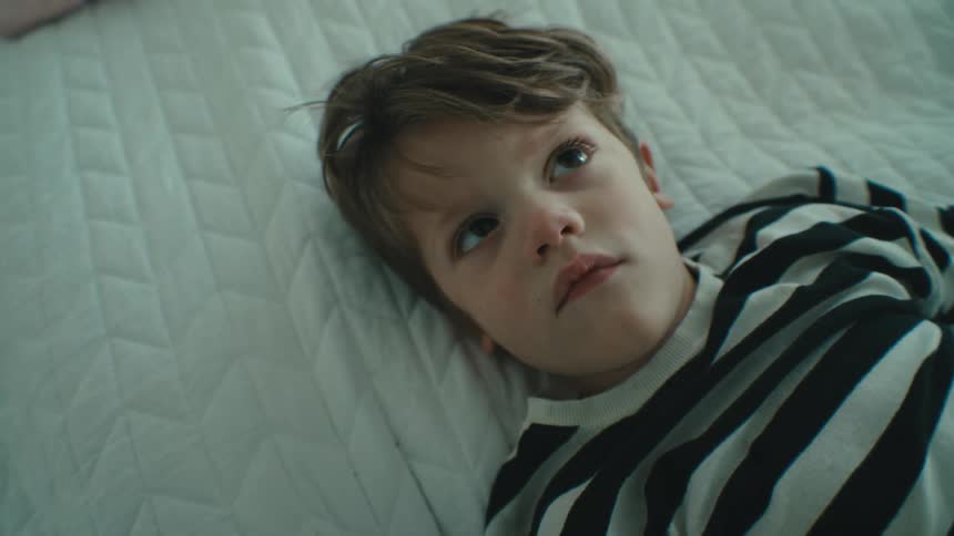 A small boy laying down on a white blanket
