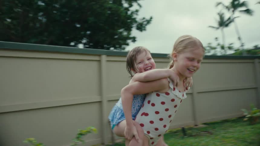 Girl wearing swimsuit carrying her little sister on her back in the backyard
