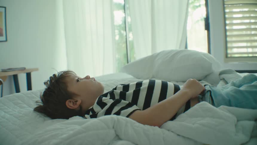 A boy lying in bed looking at the ceiling