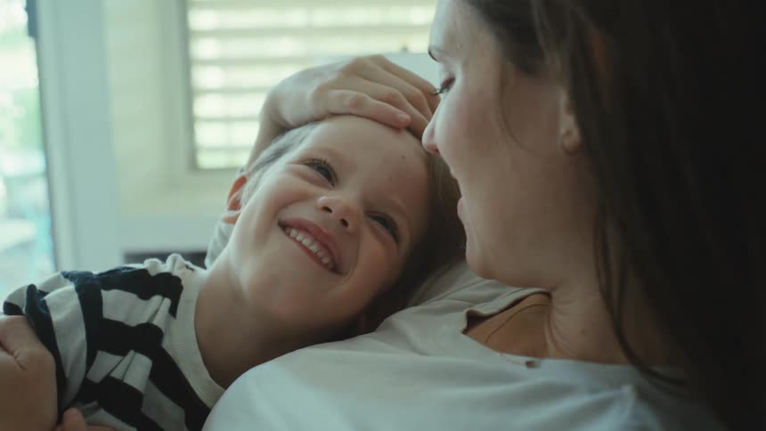 Toddler laying on the chest of her mother smiling and being caressed indoors during day time