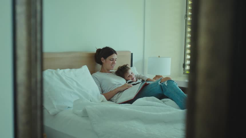 A son and mother on a bed reading a book