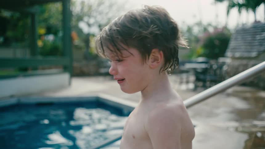 Shirtless boy crying next to a pool