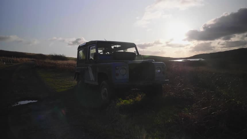 A jeep is parked in the middle of a wide open field under a cloudy sky