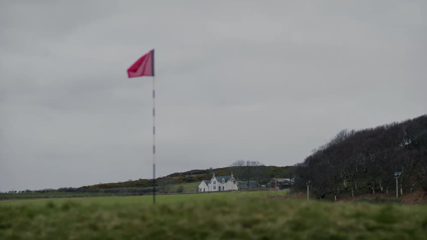 A red flag standing by the side of a grass field during the day