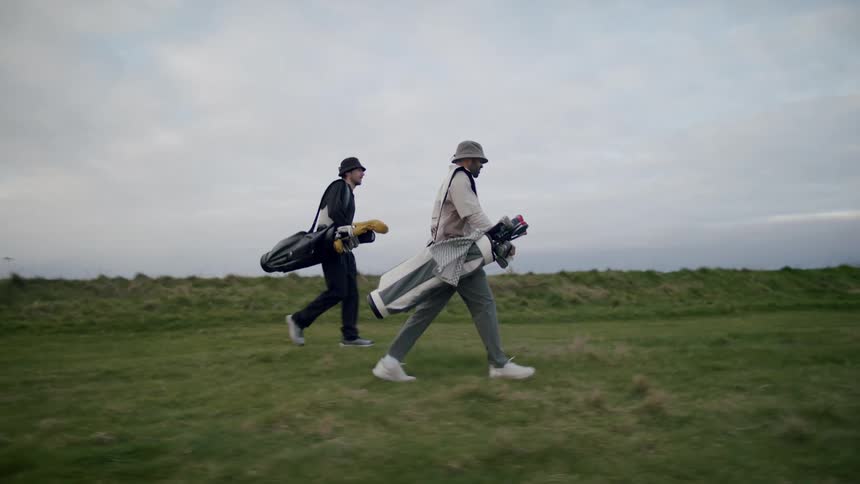 Two men carry golf bags together