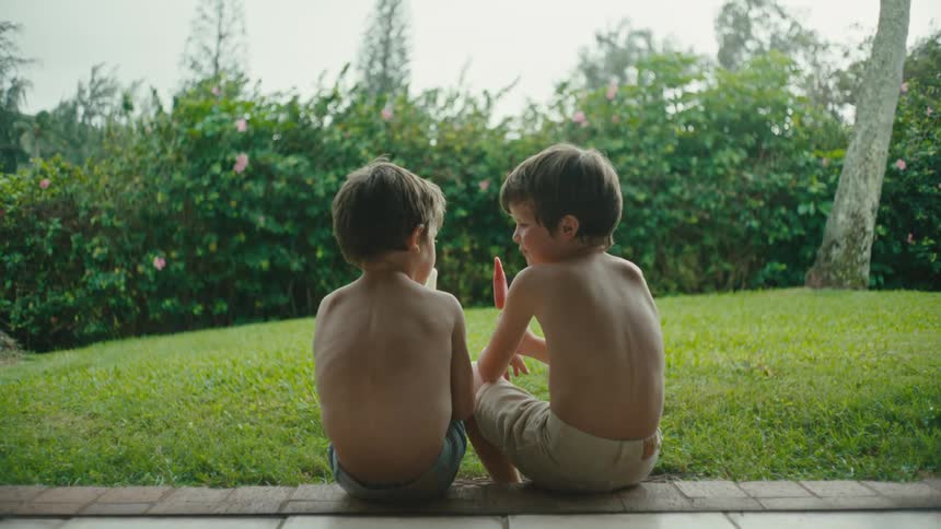Two boys sharing a popsicle outdoors on a sunny day