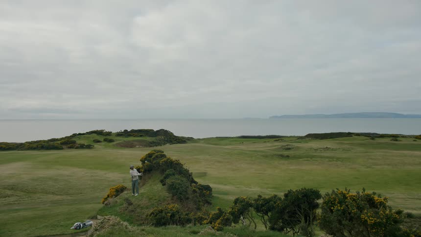 Person swings golf club standing on green outdoors cloudy day