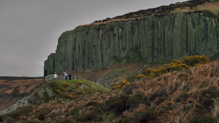 Golfer takes swing while standing on hill near base of cliff