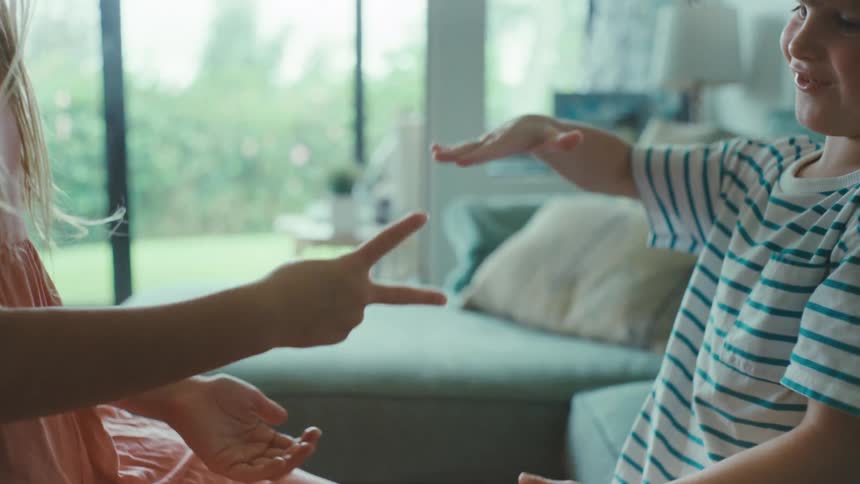 Siblings playing rock paper scissors in the living room