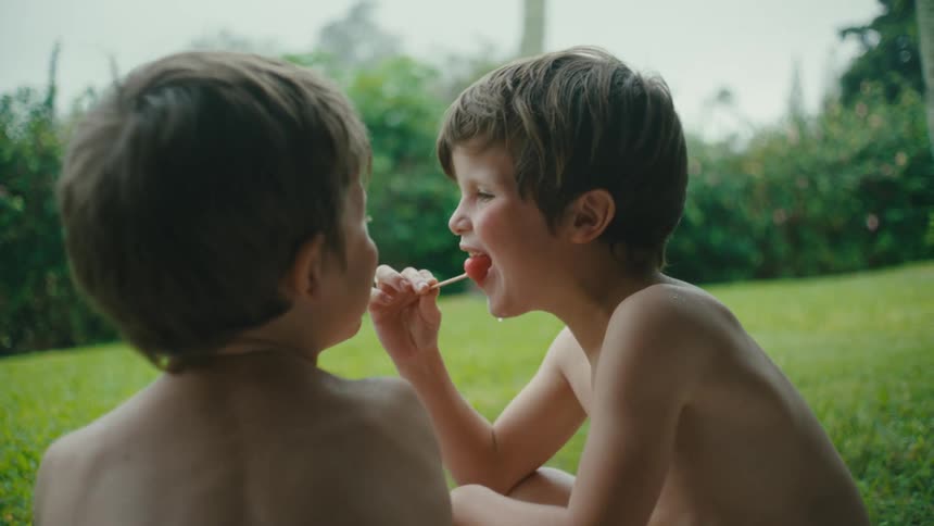 Two boys sit outside eating a popsicle