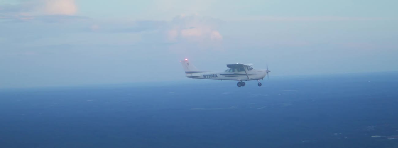 A small plane flying over the land with a cloudy sky