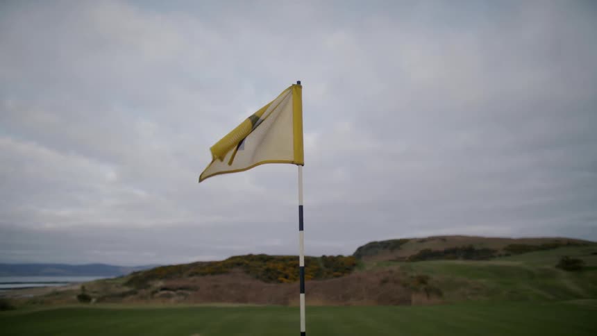 Yellow golf banner on a golf field next to a hill with water and other hills on the background on a cloudy day