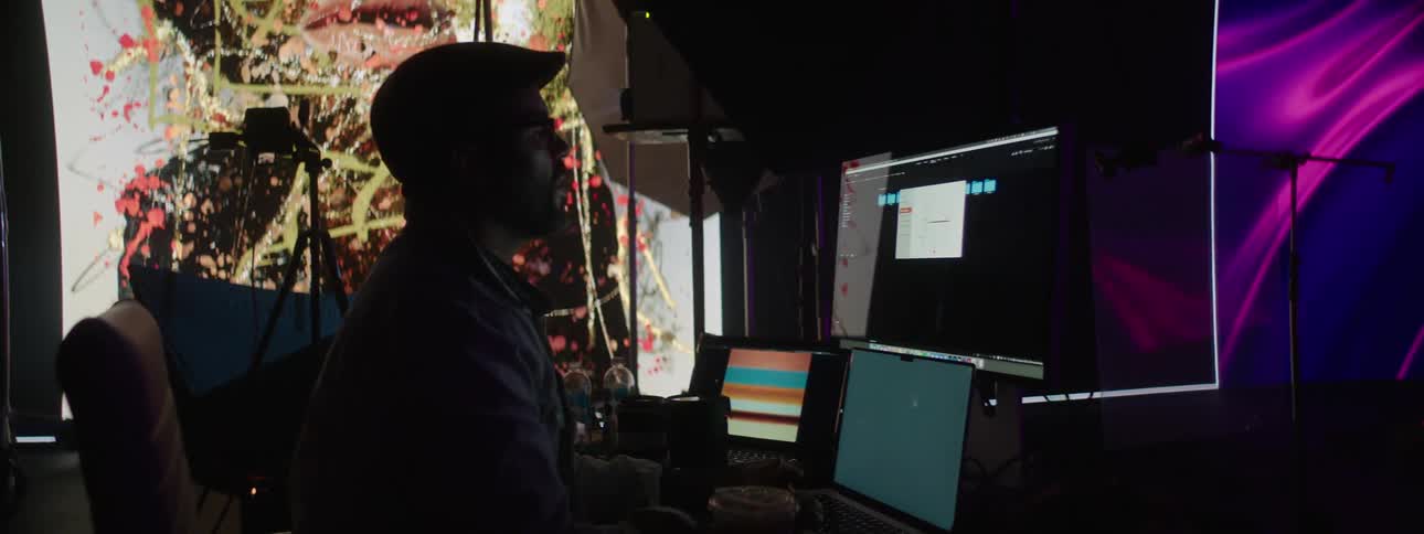 A person working on a computer in a photography set with a large projector in the background