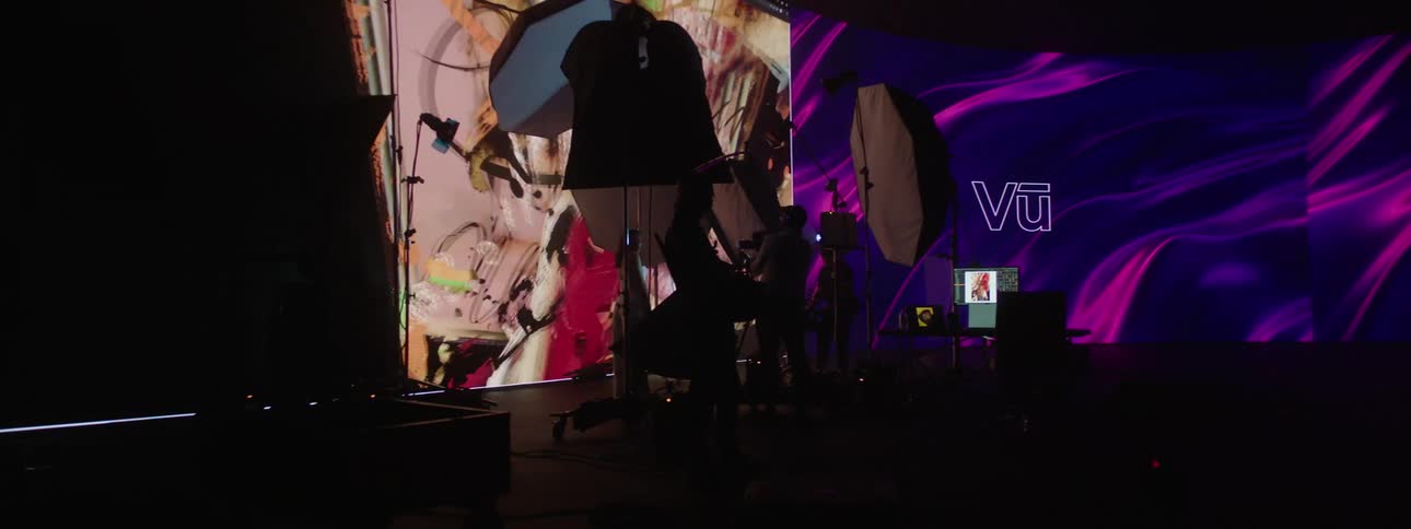 A person standing in a room with video equipment and videos playing on large screens