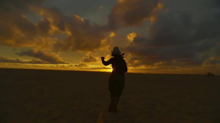 A woman runs towards the horizon during a beautiful sunset