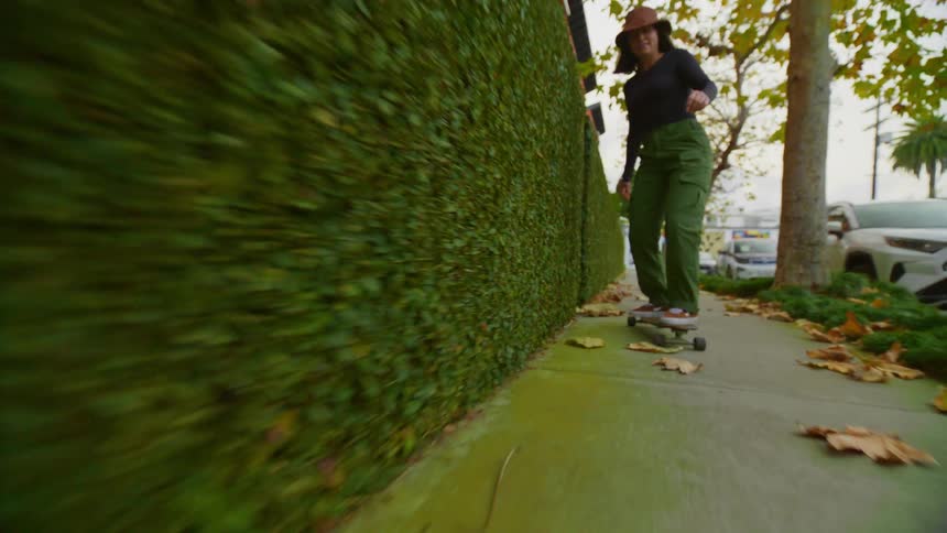 Female skateboarder rides skateboard along sidewalk at base of hedge