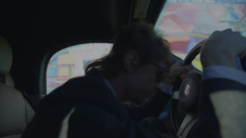 A man places his forehead on his steering wheel out of frustration