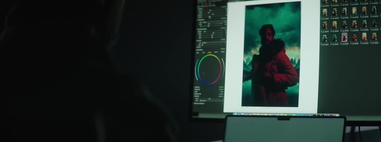 Man with glasses editing pictures on a computer in a dimly lit room