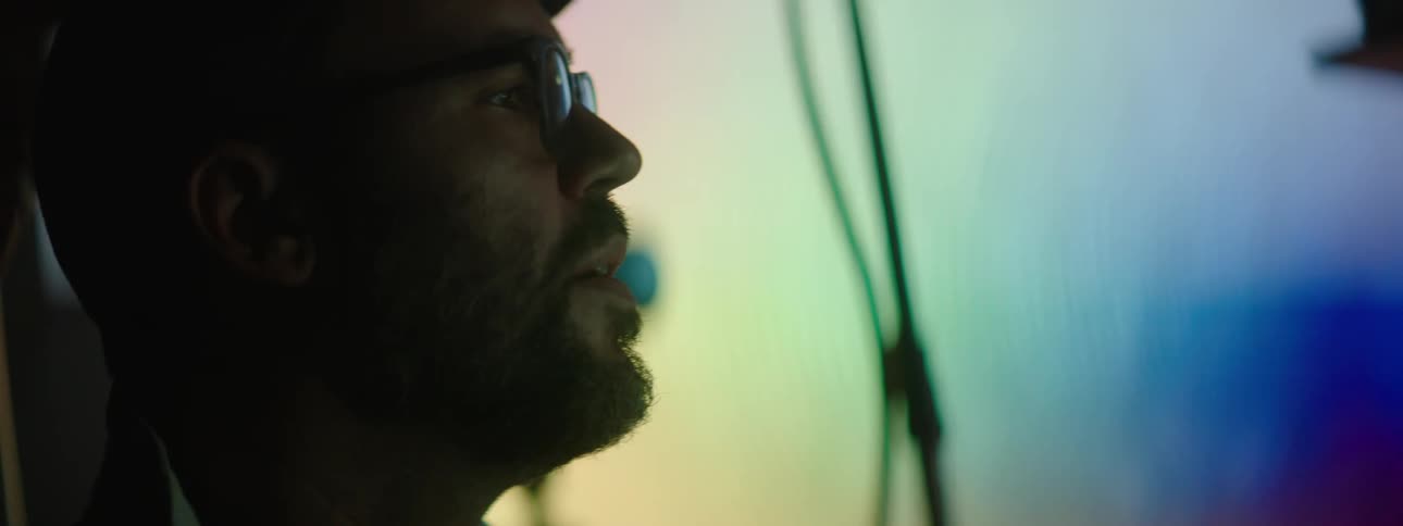 Profile of a man wearing glasses in front of a large projector