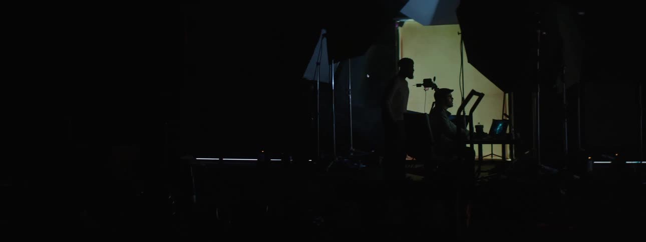 Two musician on a dark stage performing music with a blinking large screen