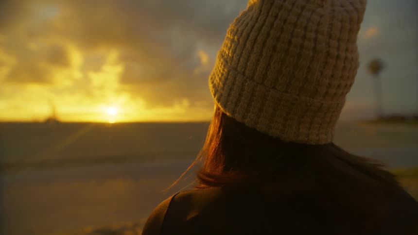 Back of the head of a woman looking at the sunset from the beach