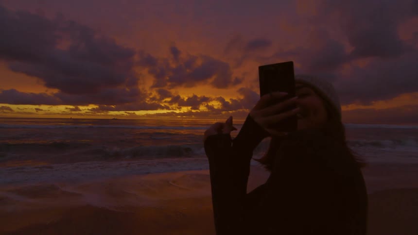 A lady at the beach taking a picture of the sea