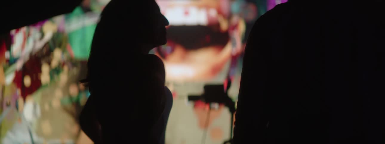 A male filmmaker looks upon a large screen with a female performer