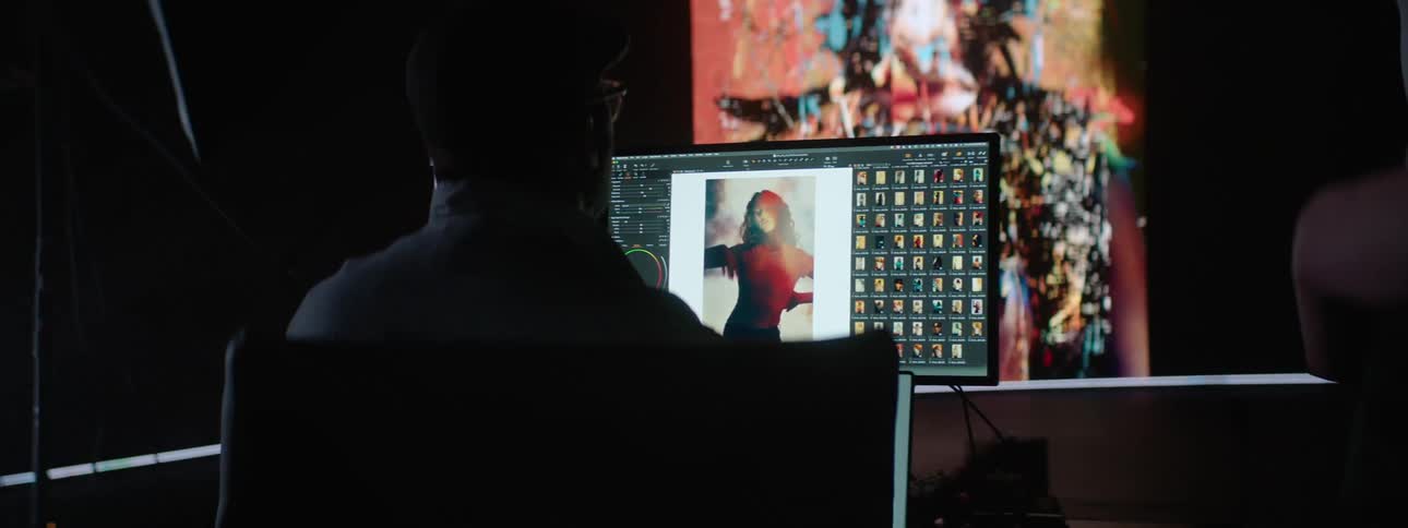 Man with glasses editing pictures on a computer in a dimly lit room