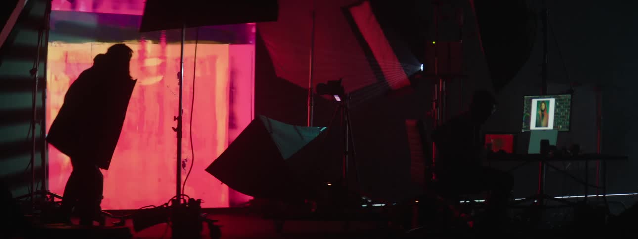 Silhouette of two people exiting from inside a dark studio room with images projected on the wall