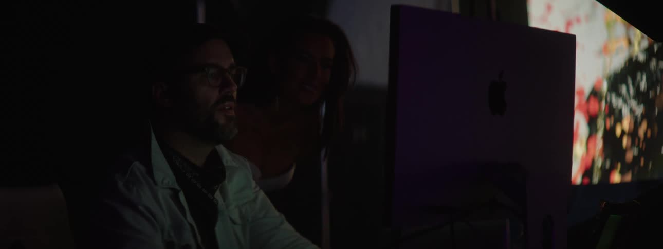 A woman looks over a colleagues shoulder while he types on his computer