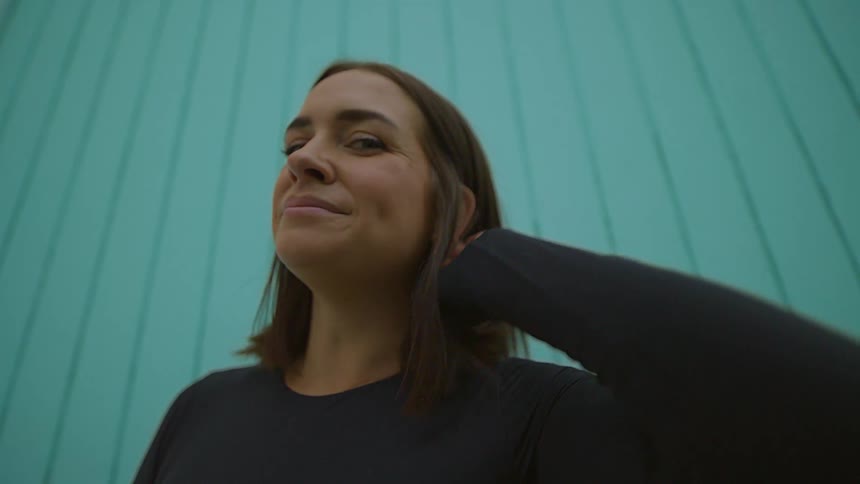 Woman smiles while standing near wall and combing back her hair