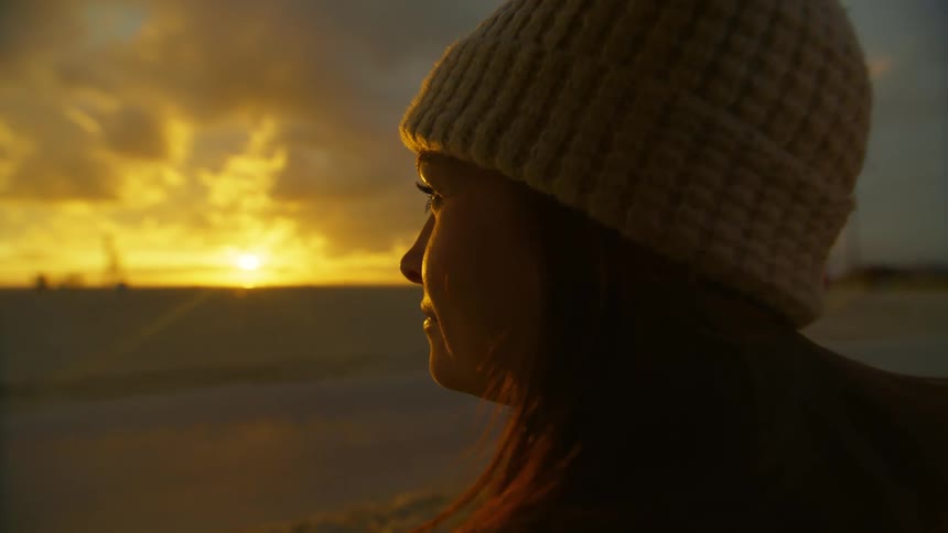 A female wearing a knitted hat in front of a sunset