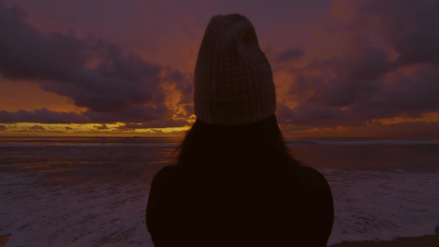 Silhouette of a woman wearing a beanie looking at the sunset from the beach