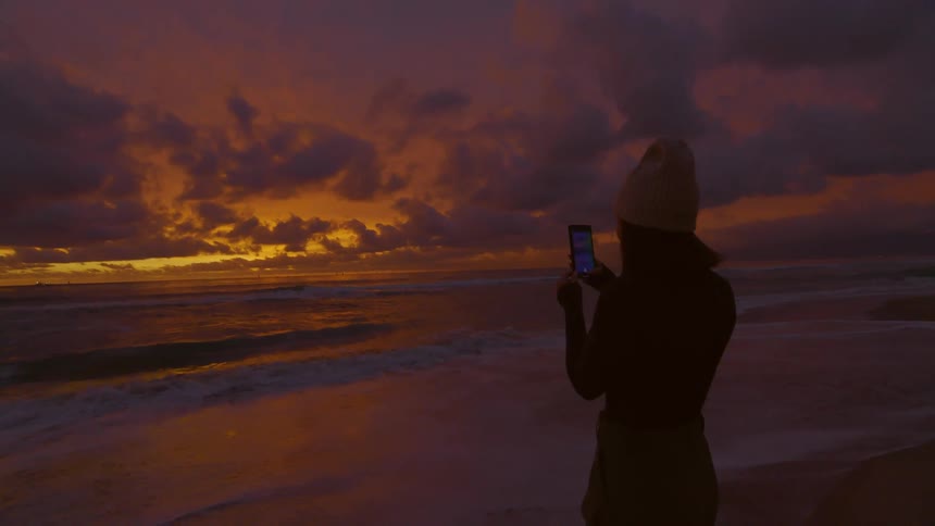 A clip of a woman taking a photo of the beach waves