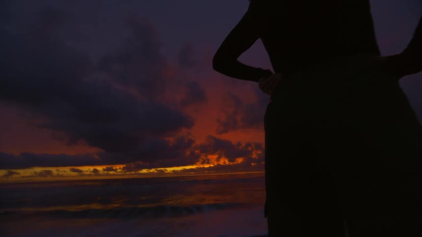 A woman is on the beach watching the sunset