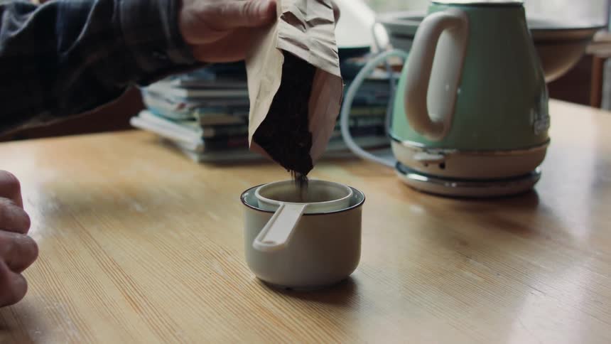 A man pours loose tea into a filter and prepares to pour hot water over it