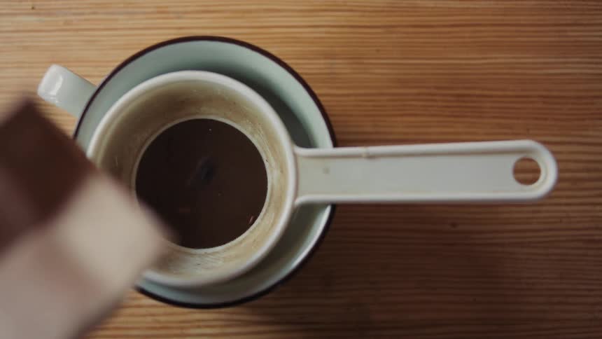 A had shakes tea leaves from a paper bag into a strainer in a mug