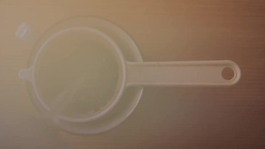 Steaming hot water is poured over tea leaves in a filter atop a cup