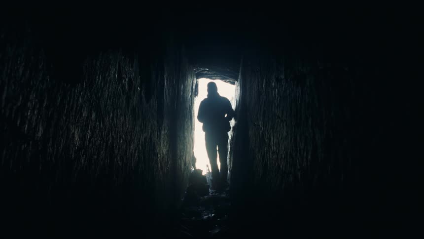 A person is entering a cave with smooth walls and lights a flashlight to be able to see